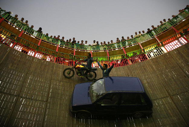 People watch as an Indian stuntman rides a motorcycle as another drives a car across a vertical wall at the Mahim fair in Mumbai, India, Tuesday, Dec. 29, 2015. The ten days-long fair that is held annually in honor of 13th century Sufi saint Makhdoom Ali Mahimi. 