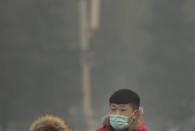 People wearing face masks walk across Tiananmen Square on a day with poor air quality in Beijing, Saturday, Nov. 28, 2015. 