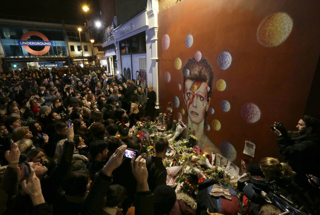 People gather next to tributes placed near a mural of British singer David Bowie by artist Jimmy C, in Brixton, south London, Monday, Jan. 11, 2016. Bowie, the other-worldly musician who broke pop and rock boundaries with his creative musicianship, nonconformity, striking visuals and a genre-spanning persona he christened Ziggy Stardust, died of cancer Sunday aged 69. He was born in Brixton. 